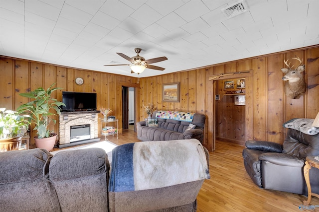 living room with ceiling fan, a stone fireplace, and light hardwood / wood-style flooring