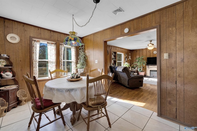 dining space with wooden walls, light tile patterned floors, and ceiling fan