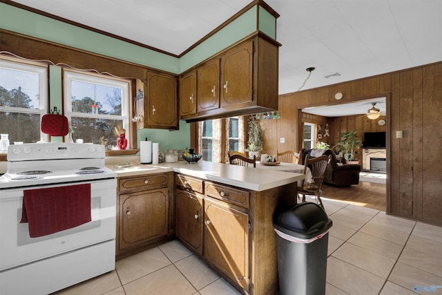 kitchen with white range with electric cooktop, wood walls, kitchen peninsula, and light tile patterned flooring