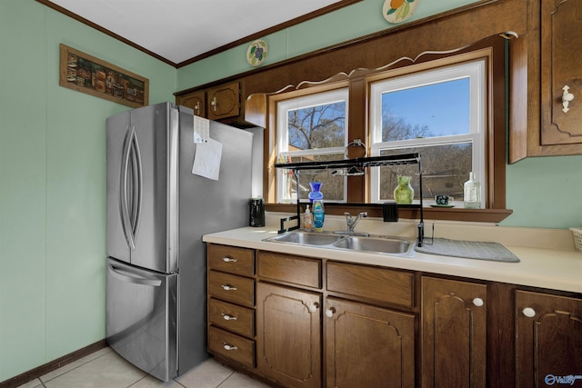 kitchen featuring sink, light tile patterned floors, crown molding, and stainless steel refrigerator