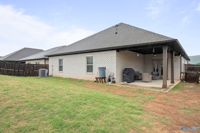 rear view of house with central air condition unit, a lawn, fence, a patio, and brick siding