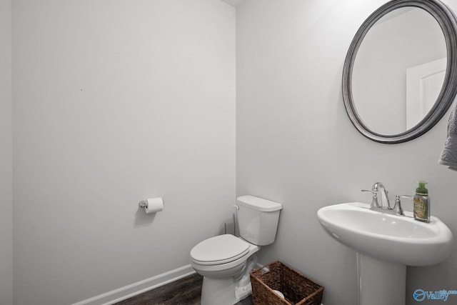 half bath featuring baseboards, wood finished floors, and toilet