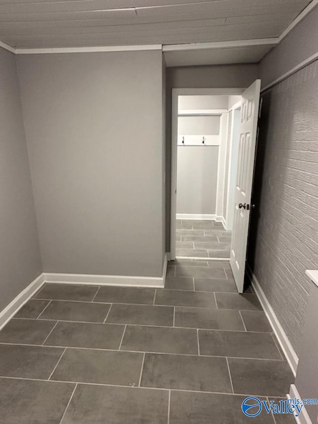 corridor featuring brick wall, dark tile patterned flooring, and ornamental molding