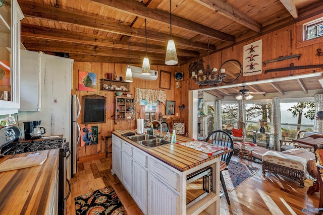 kitchen featuring sink, white cabinetry, hanging light fixtures, stainless steel appliances, and wood walls