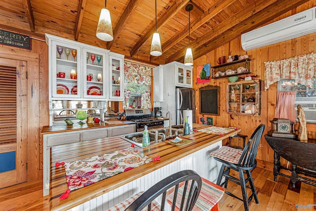 kitchen featuring pendant lighting, wooden counters, appliances with stainless steel finishes, white cabinets, and an AC wall unit