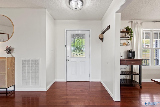 foyer featuring baseboards, visible vents, wood finished floors, and a textured ceiling