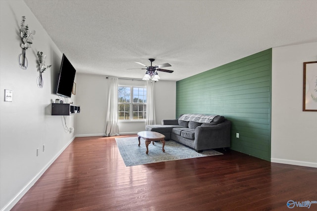 living room with an accent wall, wood finished floors, a textured ceiling, baseboards, and ceiling fan
