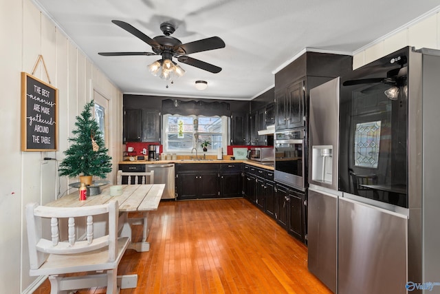 kitchen with light wood-style flooring, ceiling fan, stainless steel appliances, light countertops, and dark cabinets