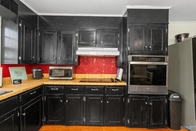 kitchen with under cabinet range hood, stainless steel appliances, dark cabinetry, and light countertops