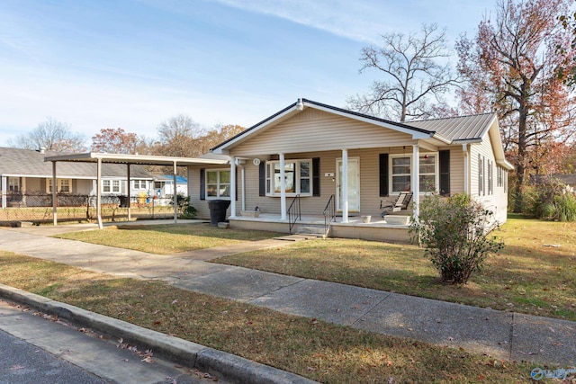 view of front facade with a front lawn, fence, covered porch, metal roof, and an attached carport