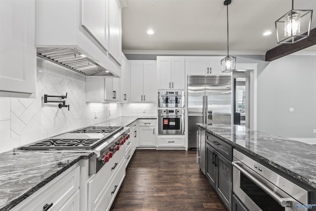 kitchen featuring white cabinetry, stainless steel appliances, dark stone countertops, and decorative light fixtures