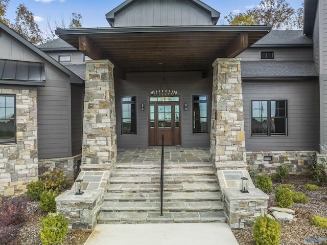 view of exterior entry featuring stone siding, a shingled roof, and board and batten siding