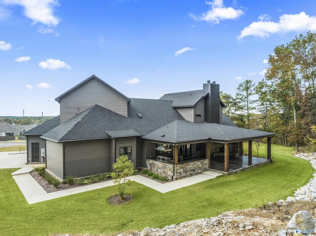 rear view of house featuring a shingled roof, a patio, exterior kitchen, and a yard