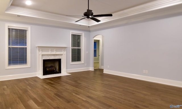 unfurnished living room with dark wood-type flooring, a fireplace, crown molding, a tray ceiling, and ceiling fan