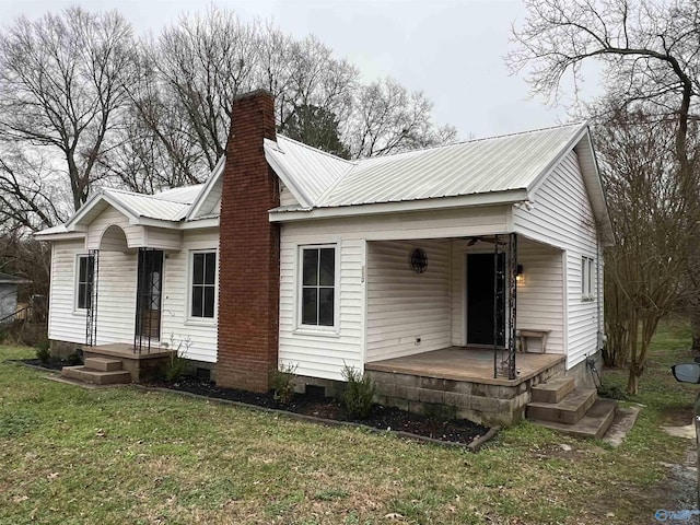 view of front of house featuring covered porch, metal roof, a front lawn, and a chimney