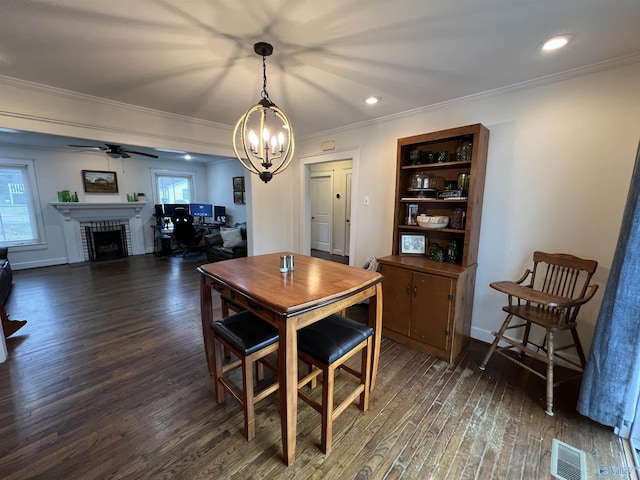 dining space with crown molding, a brick fireplace, ceiling fan with notable chandelier, and dark hardwood / wood-style flooring