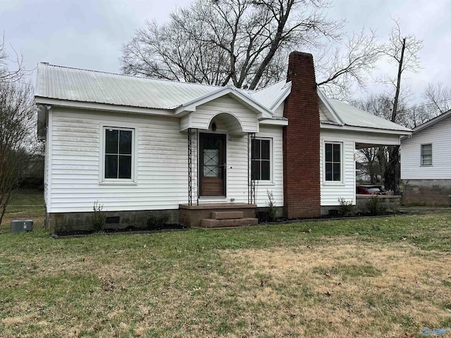 view of front of home featuring central AC, metal roof, a chimney, and a front yard