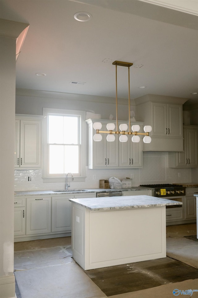 kitchen featuring a kitchen island, sink, backsplash, hanging light fixtures, and light stone counters