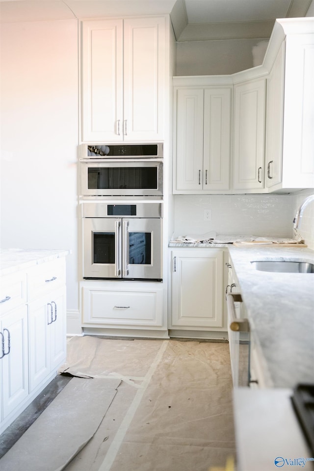 kitchen featuring sink, backsplash, white cabinets, and double oven