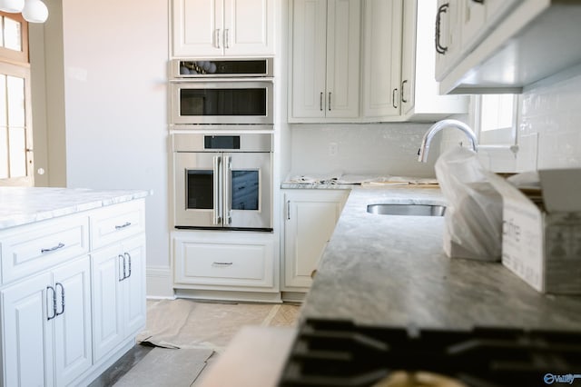 kitchen featuring sink, light stone counters, stainless steel double oven, decorative backsplash, and white cabinets