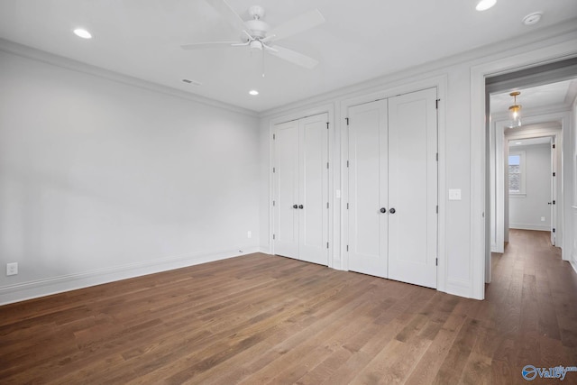 unfurnished bedroom featuring wood-type flooring, two closets, ceiling fan, and crown molding