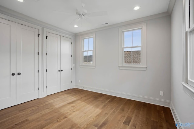 unfurnished bedroom featuring multiple closets, wood-type flooring, and ceiling fan