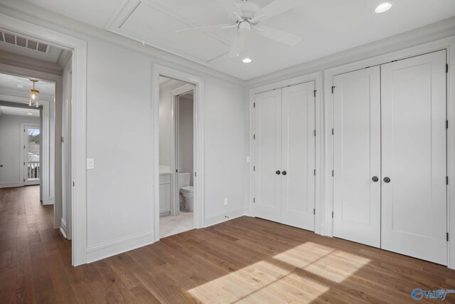 unfurnished bedroom with two closets, ensuite bath, and hardwood / wood-style flooring