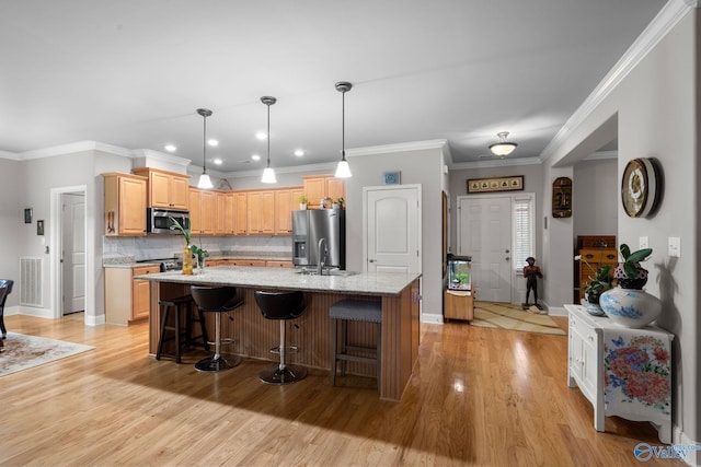 kitchen featuring appliances with stainless steel finishes, light wood-type flooring, light stone countertops, tasteful backsplash, and a center island with sink