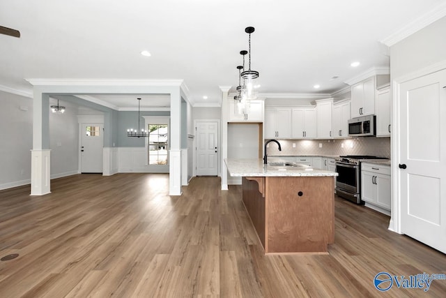 kitchen with white cabinetry, sink, stainless steel appliances, light stone countertops, and a center island with sink