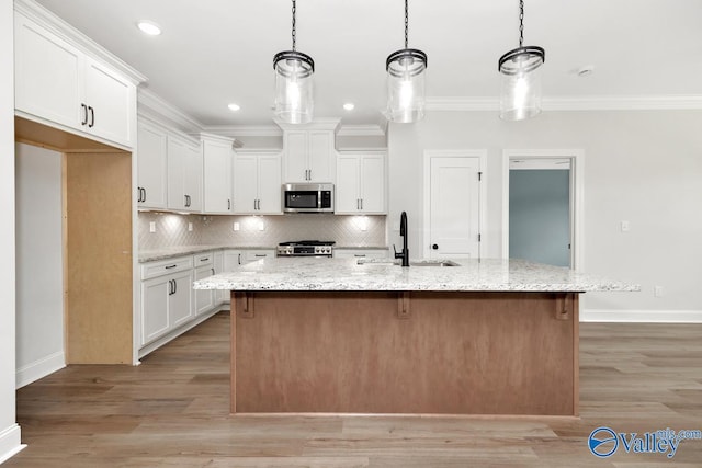 kitchen with white cabinetry, light stone counters, an island with sink, and hanging light fixtures