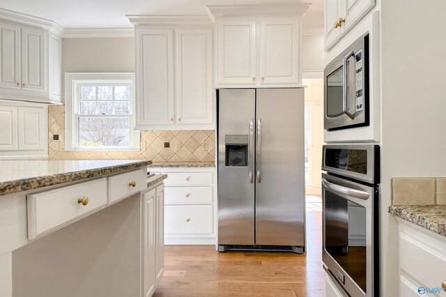 kitchen with white cabinets, light stone counters, ornamental molding, stainless steel appliances, and light wood-style floors