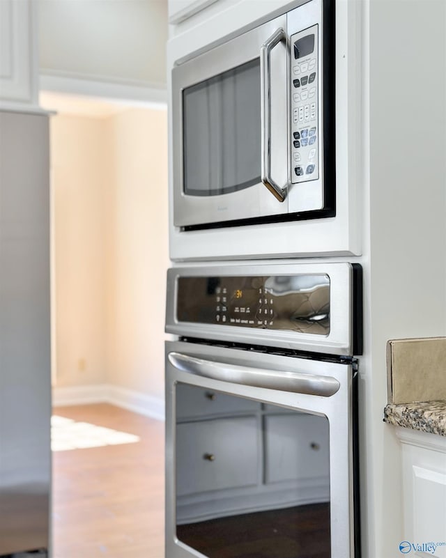 room details with wood finished floors, white cabinetry, baseboards, appliances with stainless steel finishes, and light stone countertops