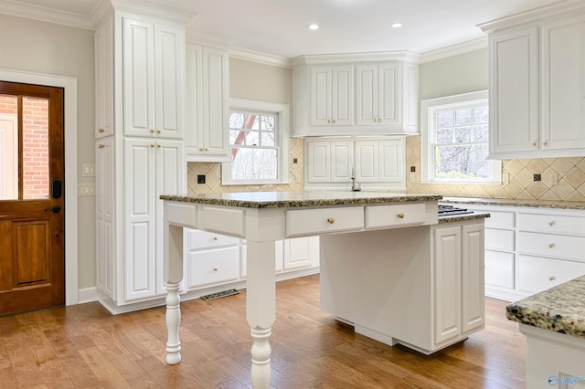 kitchen featuring light wood finished floors, a kitchen island, white cabinetry, and light stone countertops