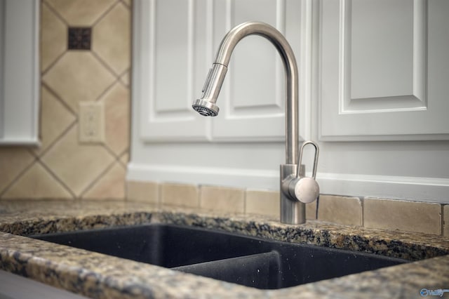 room details featuring dark stone counters, a sink, decorative backsplash, and white cabinets