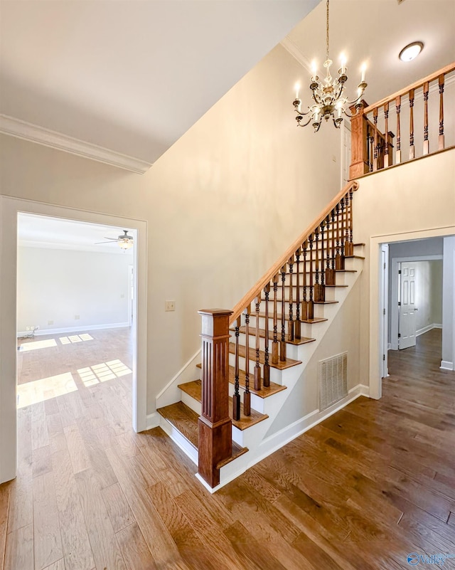 staircase featuring baseboards, visible vents, ornamental molding, wood finished floors, and ceiling fan with notable chandelier