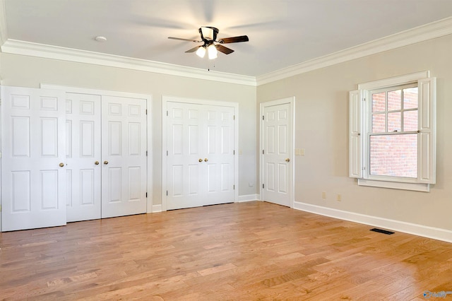 unfurnished bedroom featuring ornamental molding, light wood-style floors, baseboards, and two closets