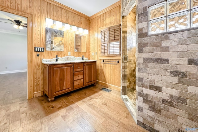 bathroom featuring double vanity, wooden walls, wood finished floors, crown molding, and a shower stall