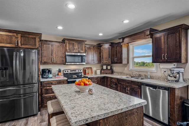 kitchen featuring a sink, dark brown cabinetry, light countertops, appliances with stainless steel finishes, and wood finished floors
