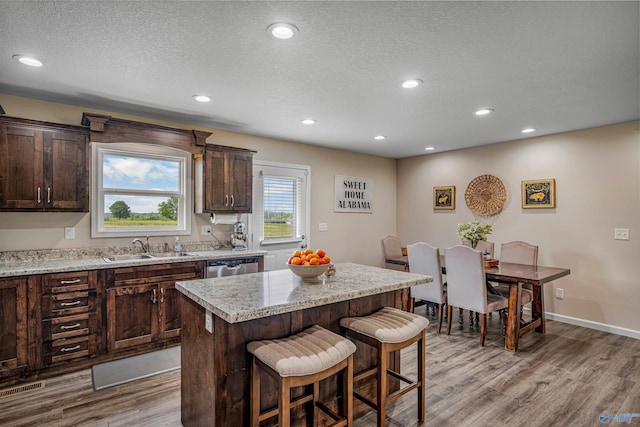 kitchen featuring a breakfast bar, dark brown cabinetry, wood finished floors, and a sink