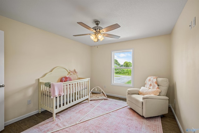 bedroom featuring a ceiling fan, a nursery area, wood finished floors, and baseboards