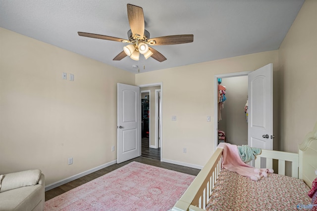 bedroom with wood finished floors, a walk in closet, a ceiling fan, and baseboards