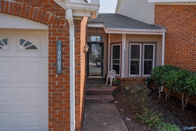 doorway to property with brick siding, an attached garage, and a shingled roof