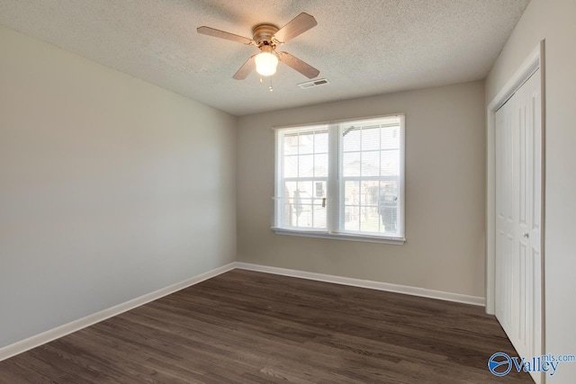 unfurnished bedroom featuring a closet, visible vents, dark wood-type flooring, a textured ceiling, and baseboards