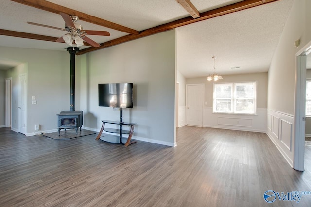 unfurnished living room featuring a wainscoted wall, wood finished floors, a wood stove, a textured ceiling, and ceiling fan with notable chandelier