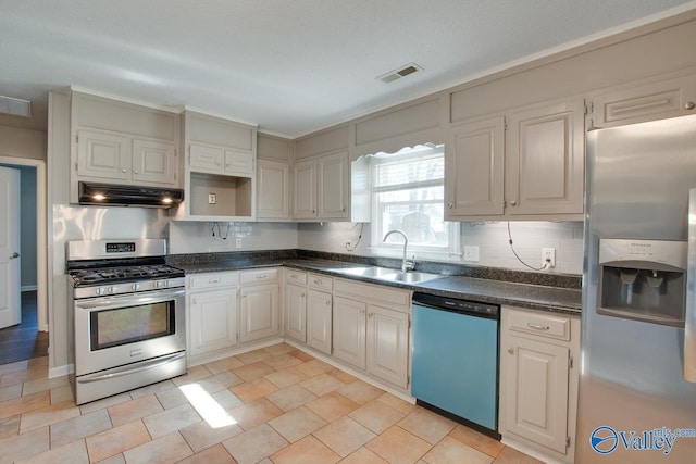 kitchen with tasteful backsplash, dark countertops, appliances with stainless steel finishes, under cabinet range hood, and a sink