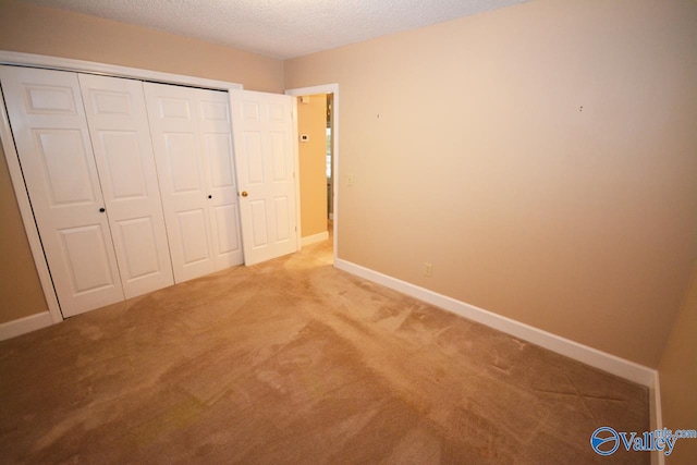 unfurnished bedroom featuring a textured ceiling, a closet, and light colored carpet