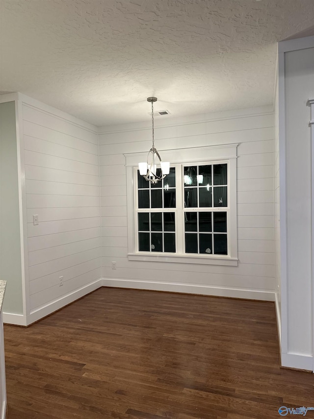 unfurnished dining area featuring a chandelier, a textured ceiling, dark wood-style flooring, visible vents, and baseboards