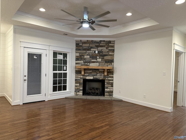 unfurnished living room with a stone fireplace, a tray ceiling, and wood finished floors