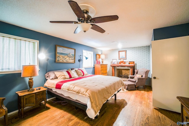 bedroom featuring ceiling fan, a brick fireplace, hardwood / wood-style flooring, and brick wall