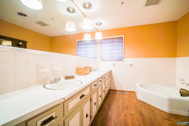 bathroom featuring a bath, backsplash, dual bowl vanity, tile walls, and wood-type flooring